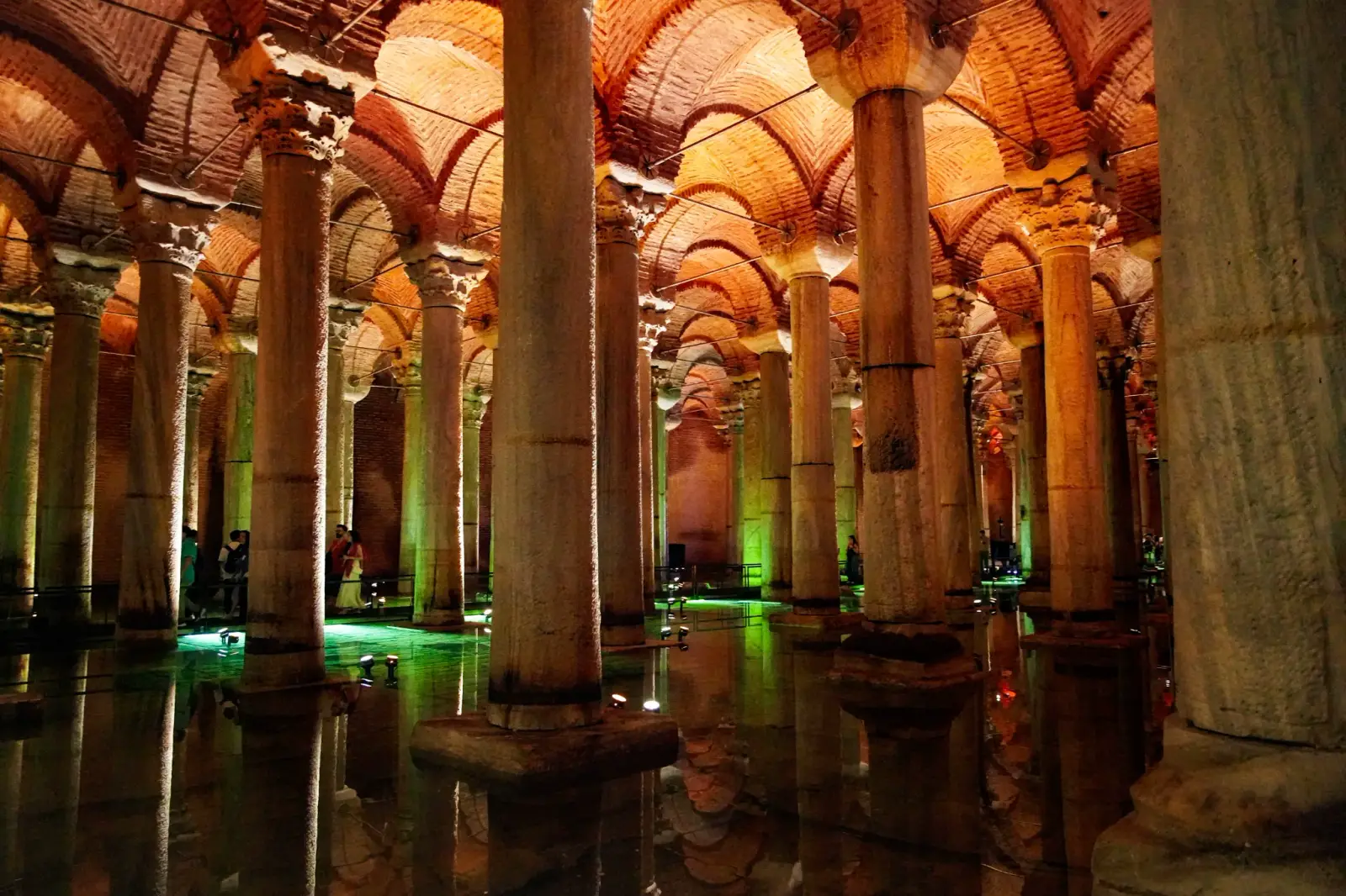 Columns of several different orders standing in the flooded chamber, green uplight across the water.