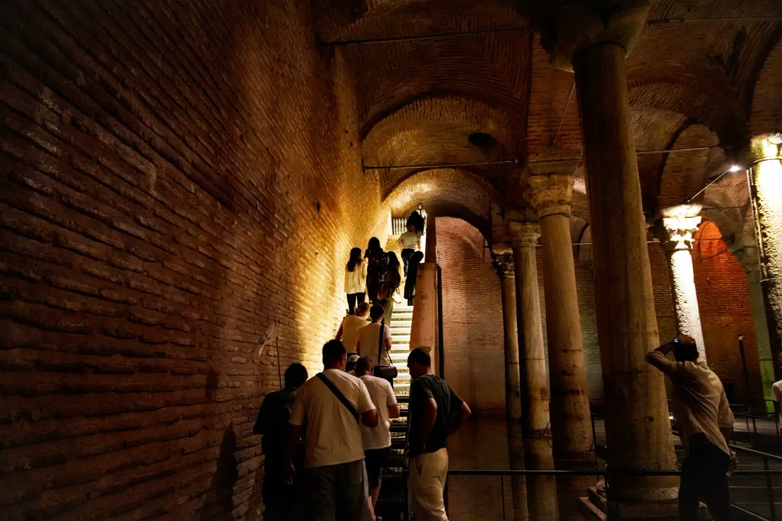 Visitors climbing the exit stair, light washing along the curved brick wall beside them.
