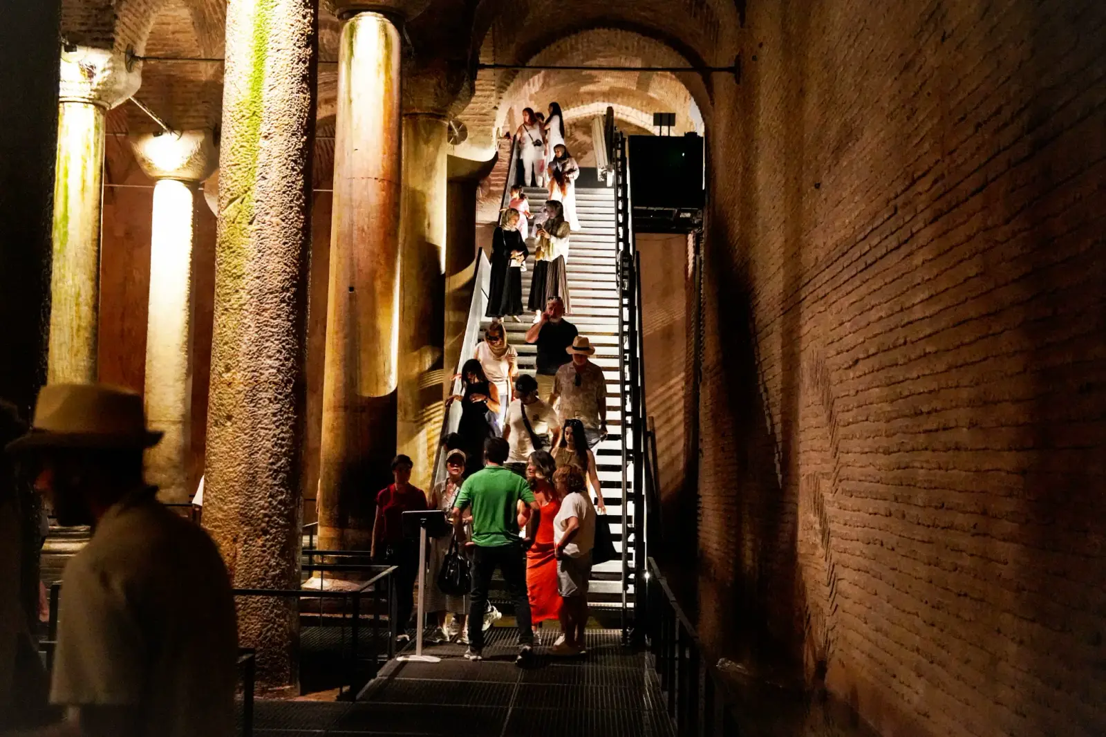 Visitors coming down the long staircase into the cistern, the brick wall of the shaft lit beside them.