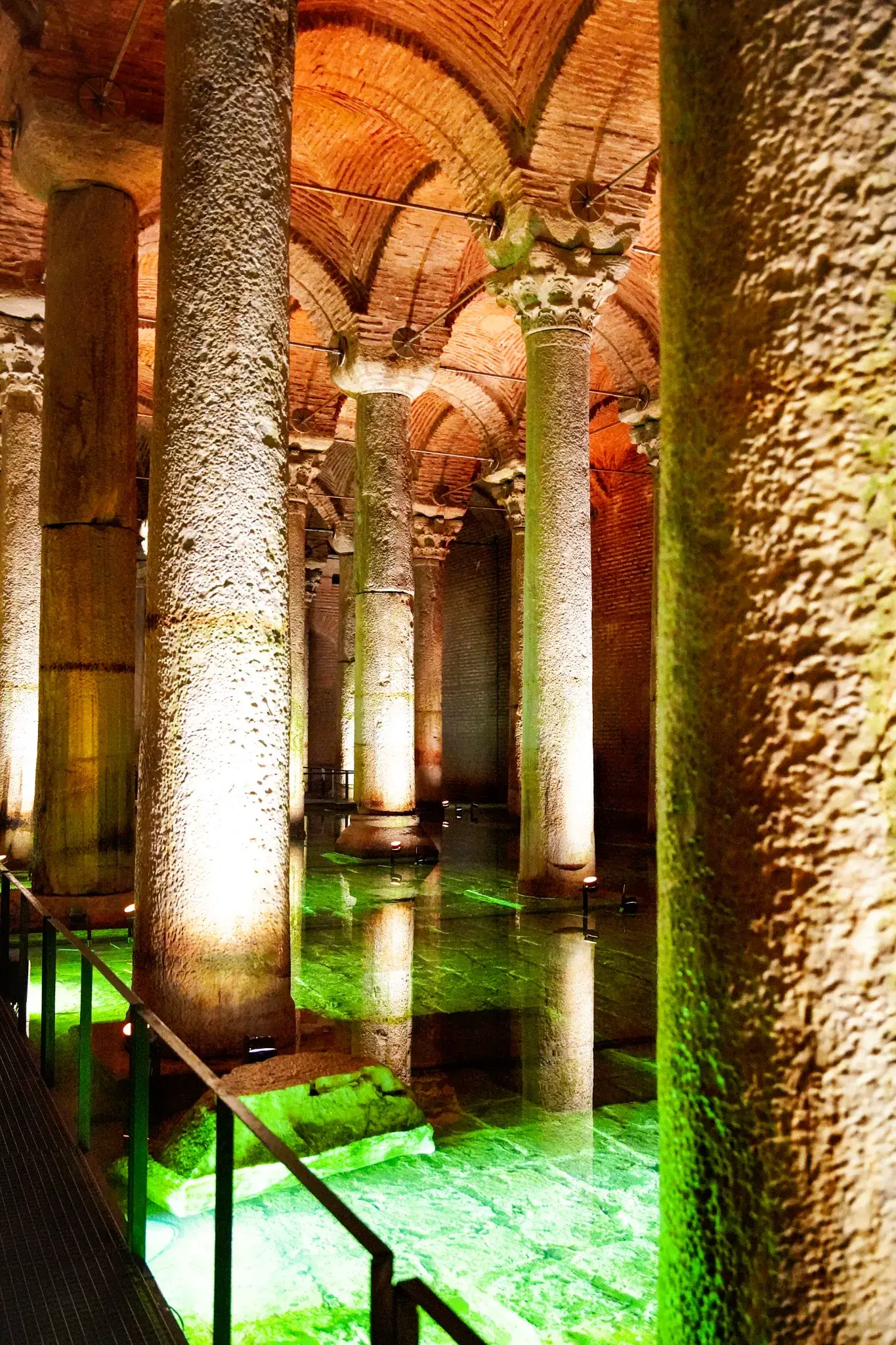 Marble shafts rising from green-lit water, the brick vaults overhead and the visitor rail in the foreground.